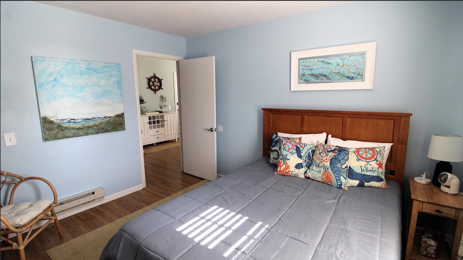 Second bedroom with a queen bed, soft blue walls, and coastal art