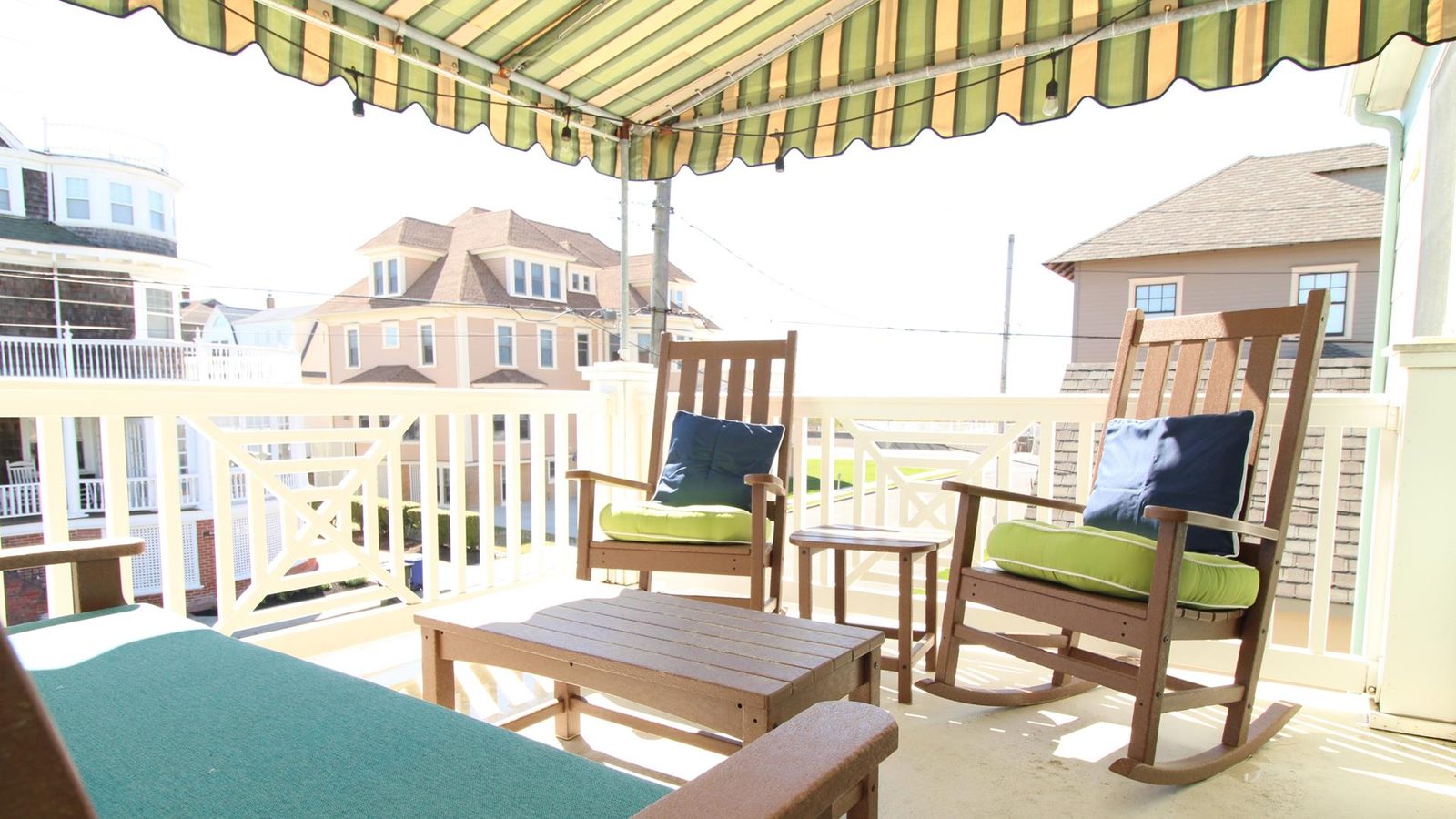Shared covered porch with rocking chairs, striped awning, and string lights